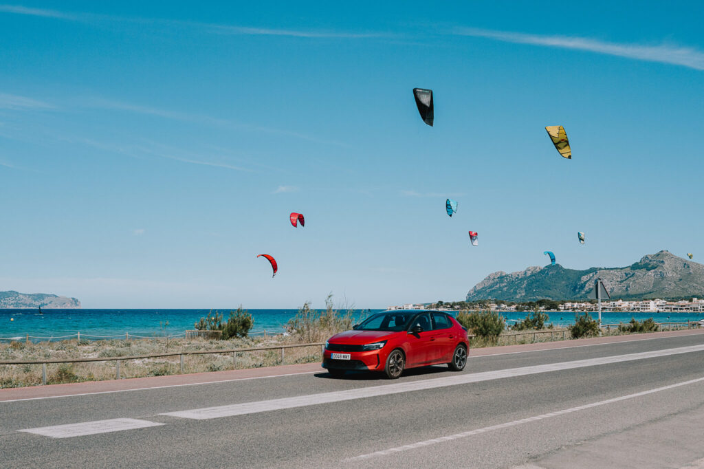 Red car driving along the road protected by car hire excess insurance with paragliders in the sky.