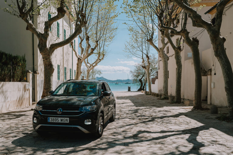 Black Volkswagen with car hire excess insurance parked on a residential road with view of the sea in the background.