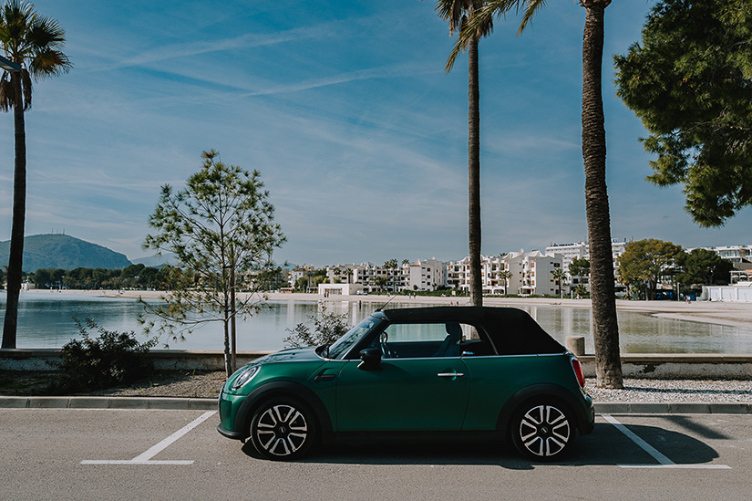 Green mini covered with rental car excess insurance parked in a carpark by the beach.