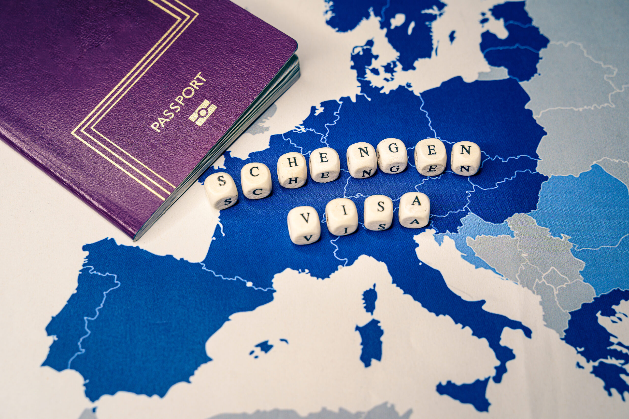 Purple passport and letter tiles spelling 'Schengen Visa' are placed on a blue map of Europe.